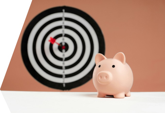 Ein Sparschwein, hinter dem eine Dartscheibe hängt.